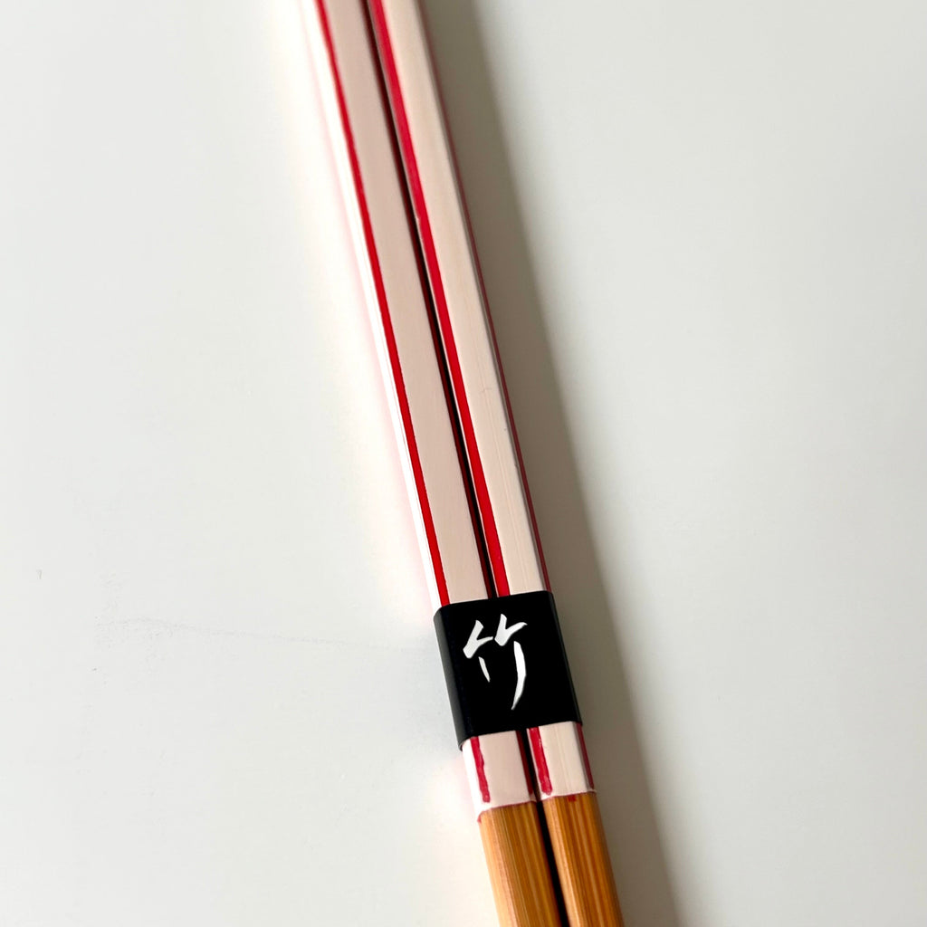 Pair of wooden chopsticks with a black band featuring a logo on a light gray background