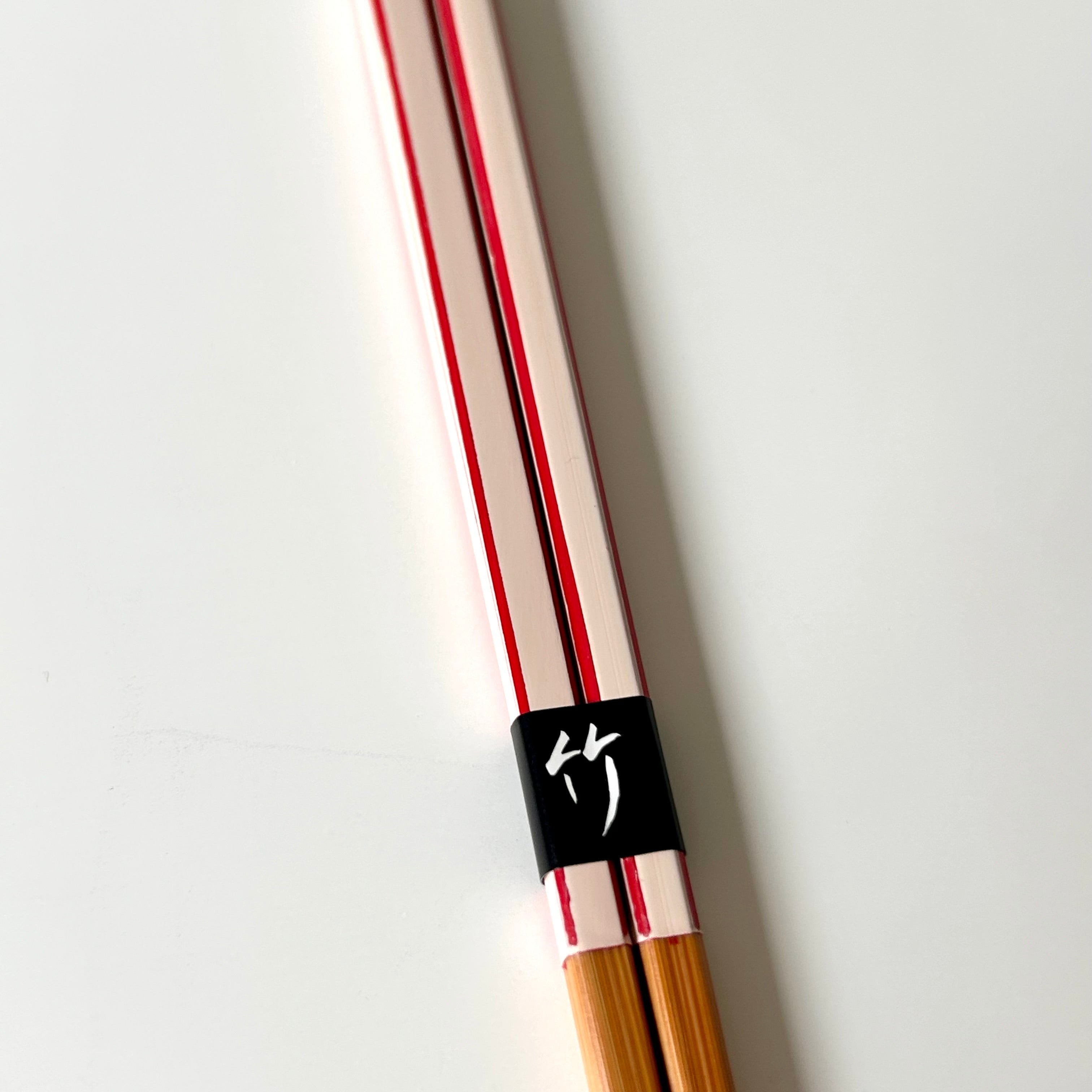 Pair of wooden chopsticks with a black band featuring a logo on a light gray background