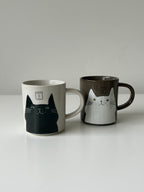 Two mugs with cat designs on a plain background