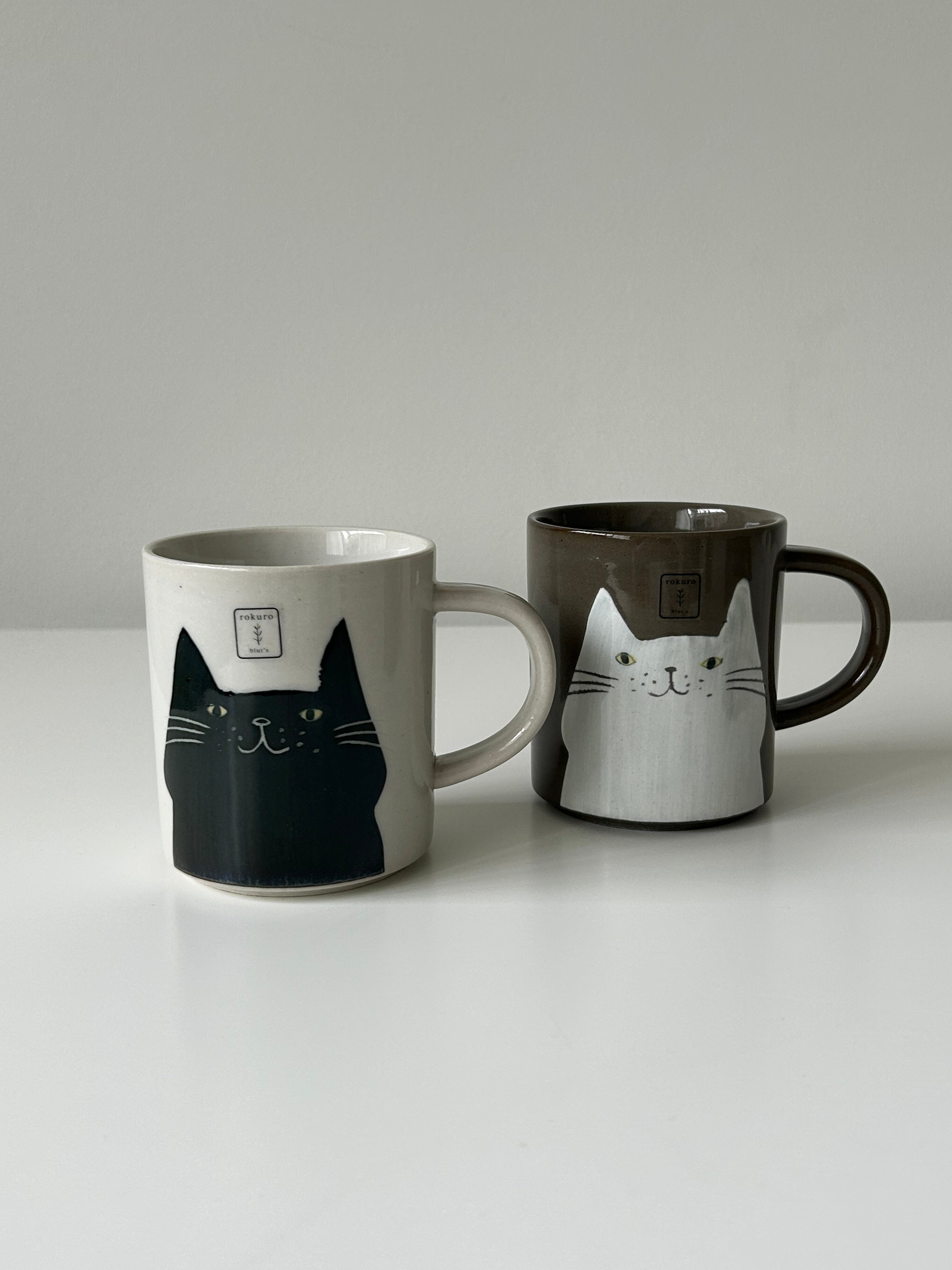 Two mugs with cat designs on a plain background
