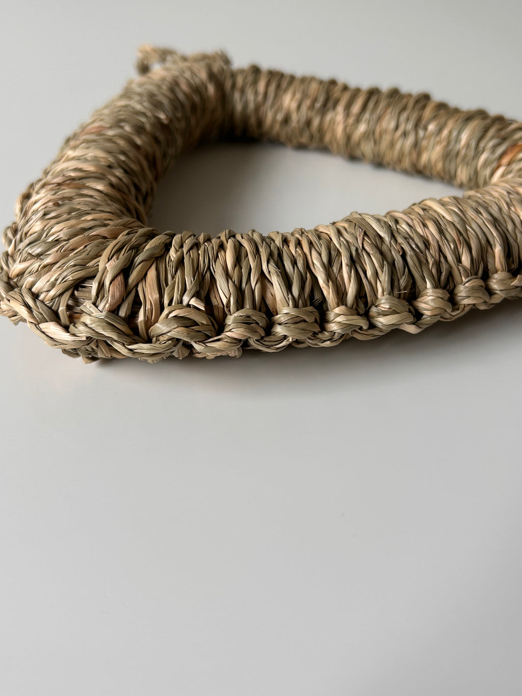 Woven seagrass heart-shaped object on a light gray background