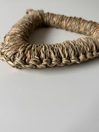 Woven seagrass heart-shaped object on a light gray background