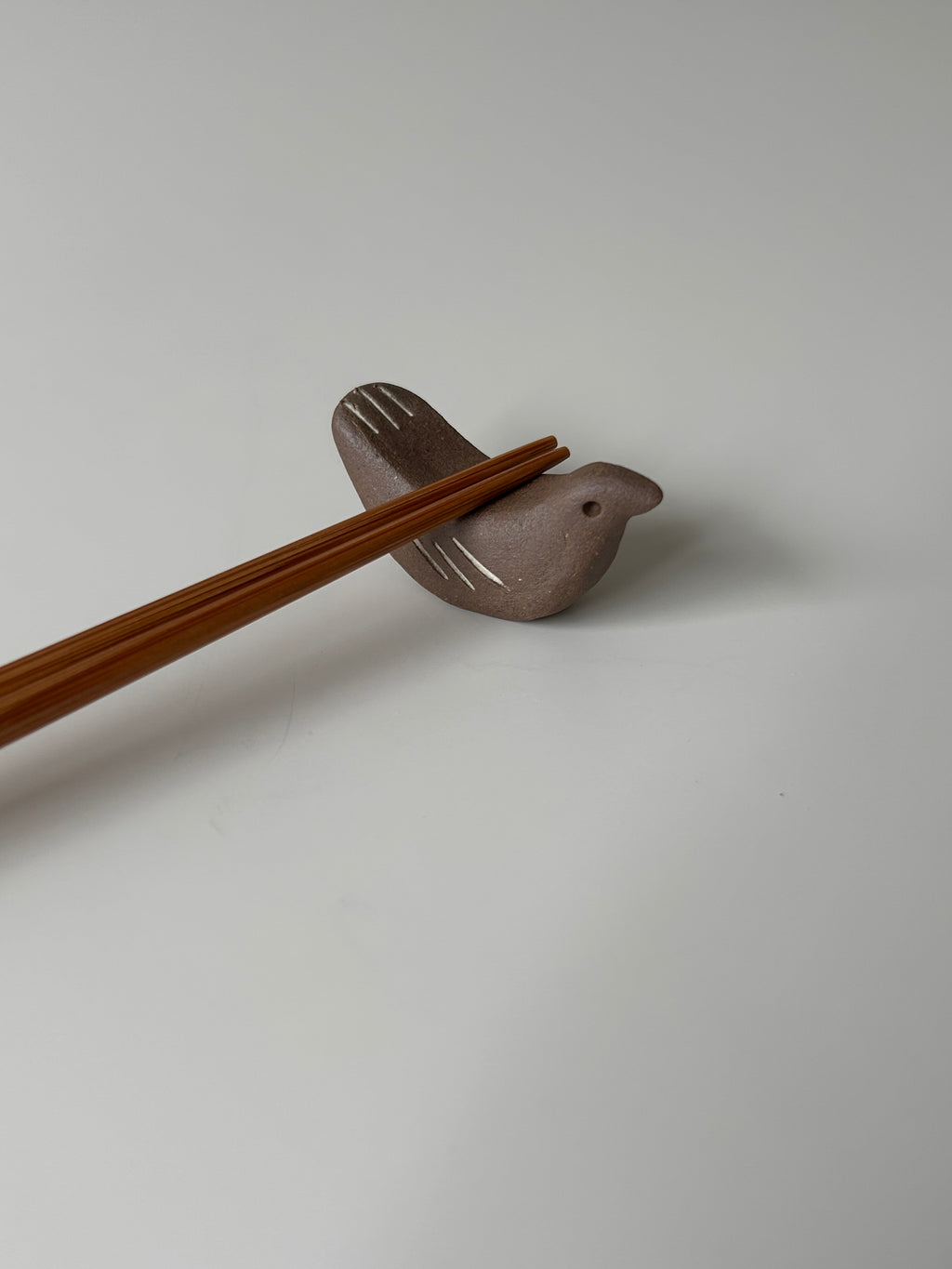 Chopstick rest shaped like a bird with wooden chopsticks on a light gray background