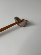 Chopstick rest shaped like a bird with wooden chopsticks on a light gray background