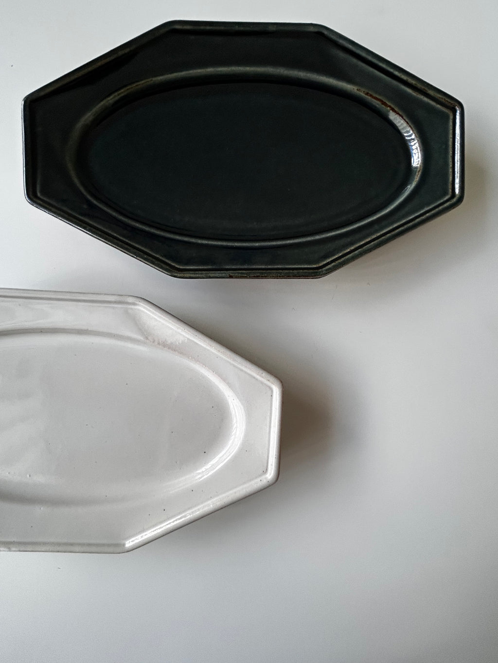 Two octagonal ceramic plates, one black and one white, on a light gray background.