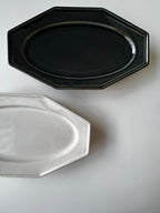 Two octagonal ceramic plates, one black and one white, on a light gray background.
